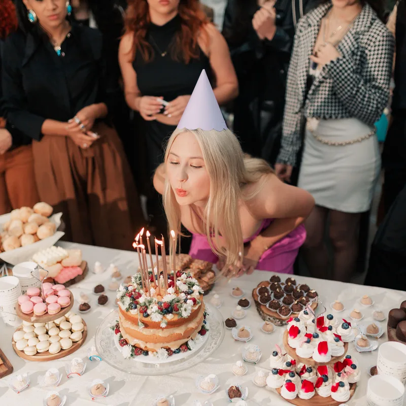 Birthday girl blowing out candles at a dessert table while friends photograph the moment for the shared album