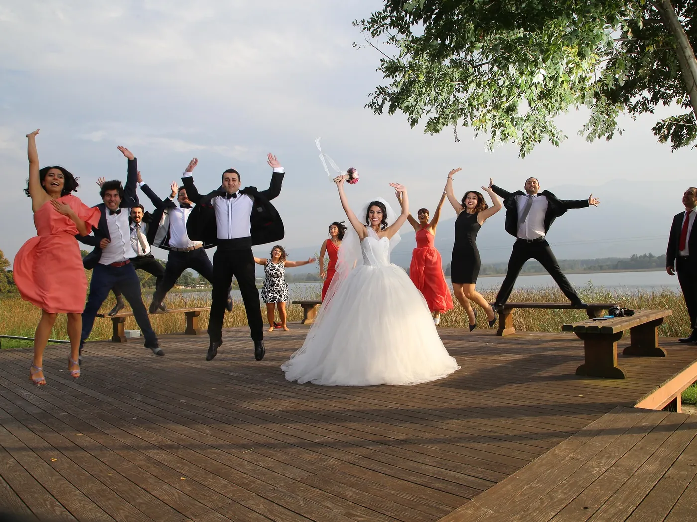 Wedding party jumping for joy around the bride on a lakeside deck